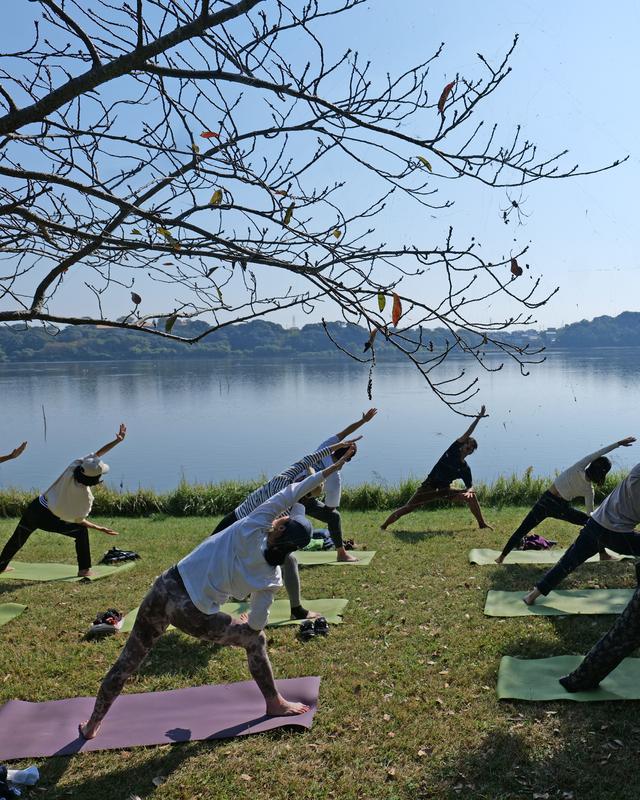 湖畔でトライアングルのポーズをとる参加者たち、色づき始めた木々と青空