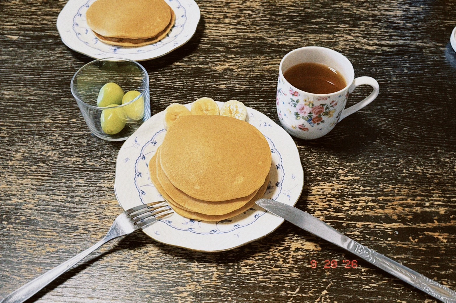 青い花柄の器に重ねた米粉パンケーキとバナナ、紅茶を添えた休日の朝食の食卓